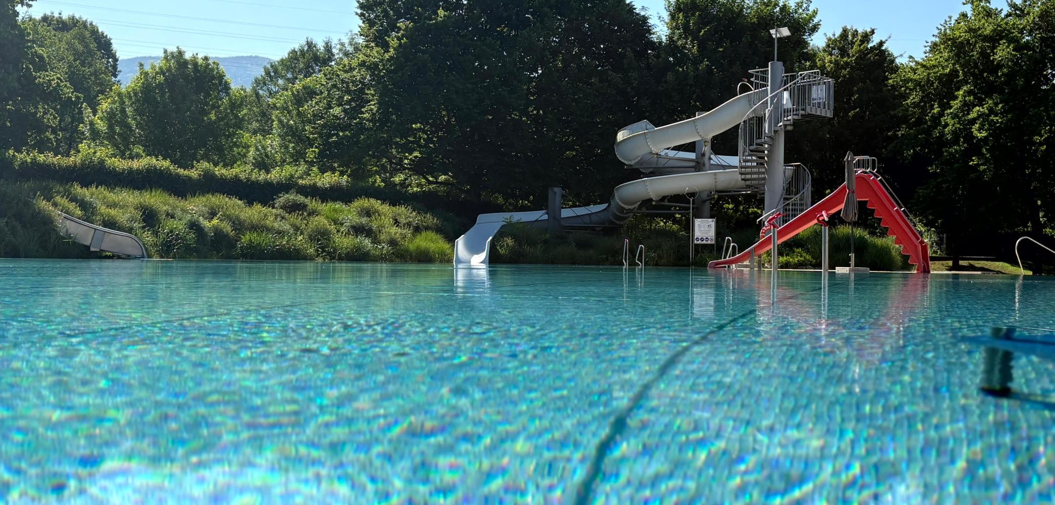 Vorne ist ein großes Schwimmbecken. Hinten sieht man zwei Rutschen.