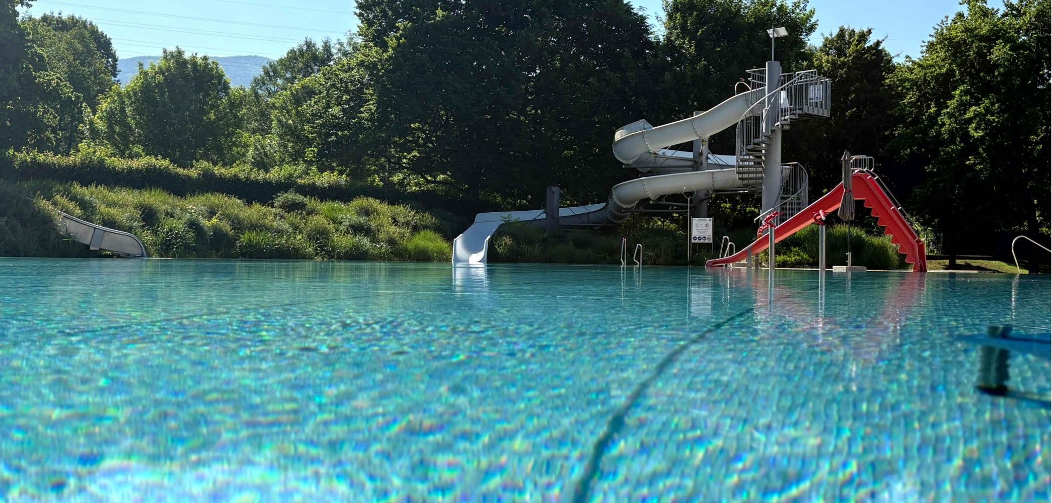 Vorne ist ein großes Schwimmbecken. Hinten sieht man zwei Rutschen.